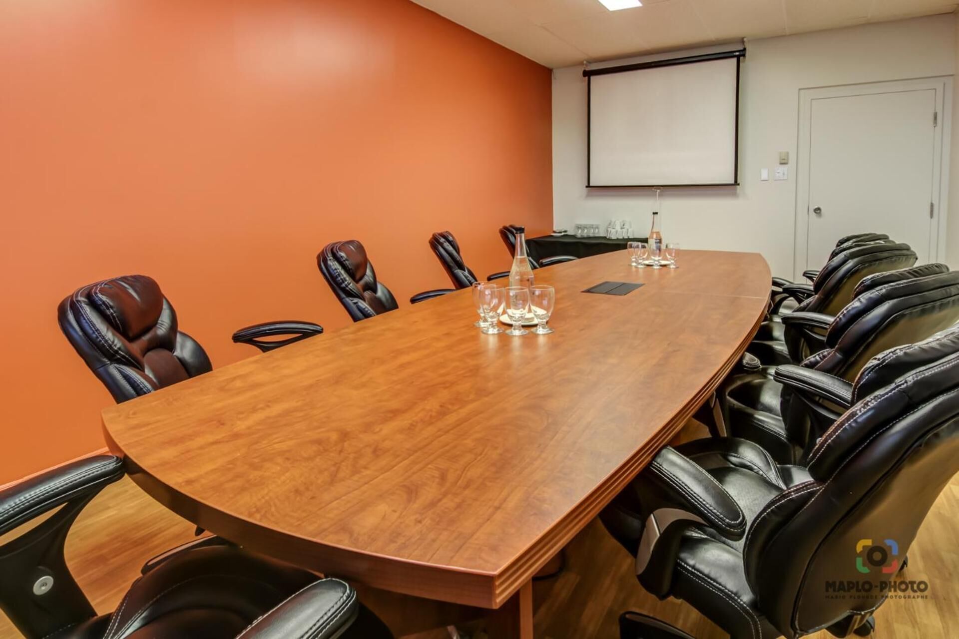 A conference room with a long wooden table, leather chairs, a projector screen, and a whiteboard.