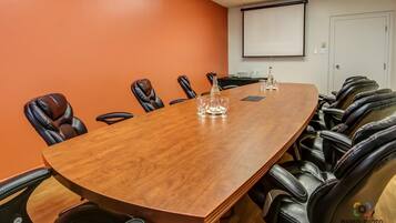 A conference room with a long wooden table, leather chairs, a projector screen, and a whiteboard.