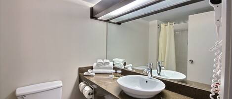 A bathroom with a white toilet, a sink with a mirror above it, and a hairdryer on the wall.