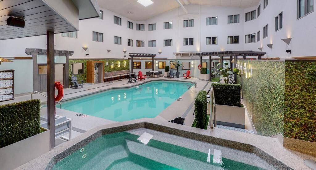 Un vestíbulo de hotel con piscina central, zonas de estar y una pared verde.