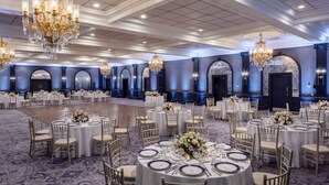 Un amplio salón de banquetes con mesas redondas dispuestas para comer, con sillas doradas y manteles blancos.