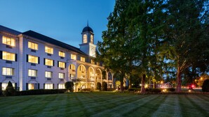 A large, multi-story building with a prominent tower and arched windows, surrounded by well-maintained lawns and trees. - Madison Hotel (Morristown)