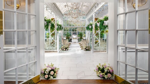 A conservatory with a glass ceiling, white walls, and a central aisle leading to a table. - Madison Hotel (Morristown)
