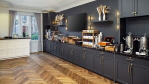 A modern kitchen with dark cabinetry, a herringbone wood floor, and a large window with curtains. - Madison Hotel (Morristown)