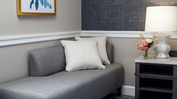 A grey sofa with two pillows, a white vase with pink flowers, and a white table lamp on a marble table.