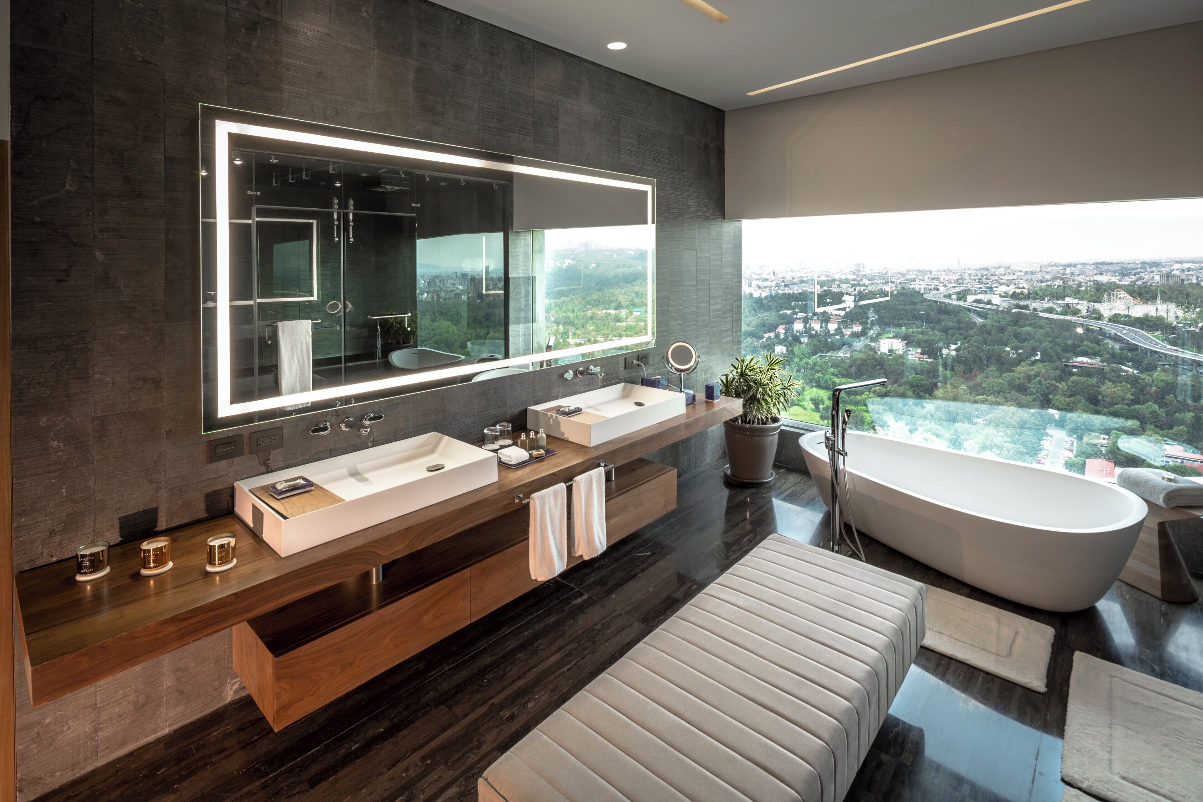 Ein modernes Badezimmer mit großem Spiegel, zwei Waschbecken, einer freistehenden Badewanne und Blick auf eine Stadtlandschaft.