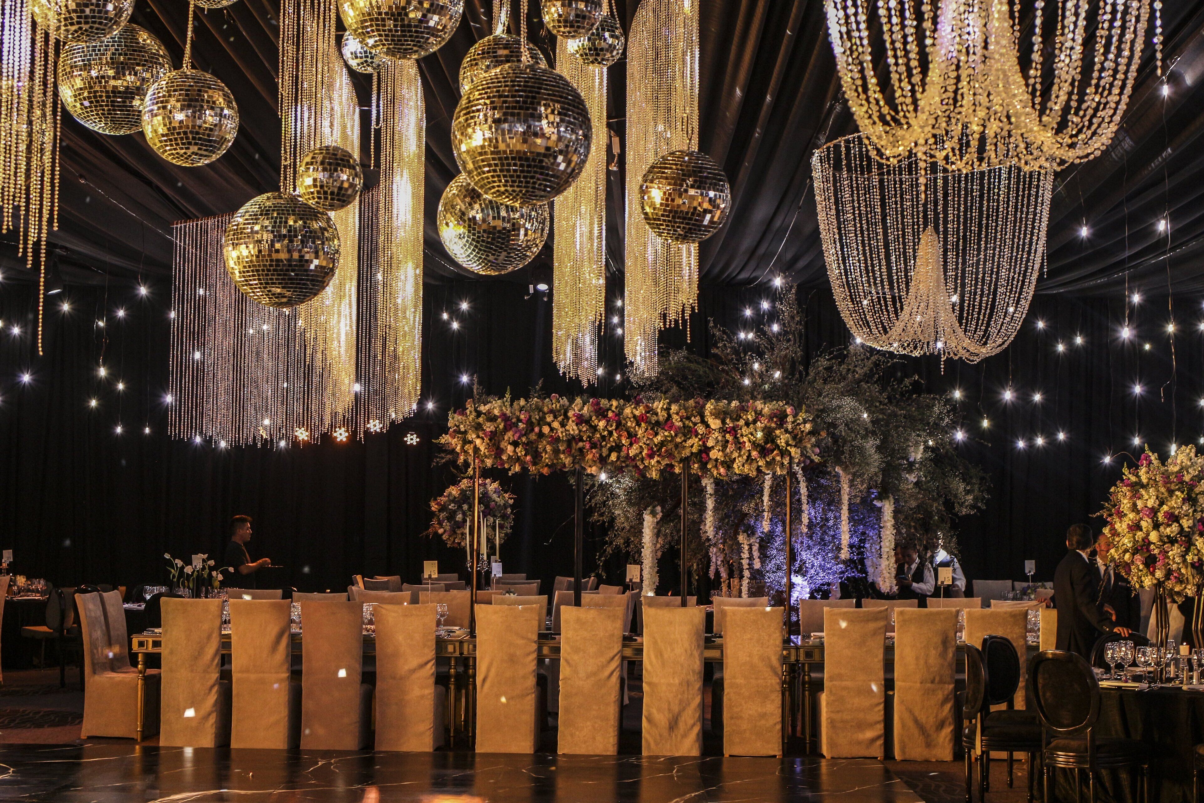 A formal event with tables set for dining, surrounded by golden disco balls and hanging decorations.