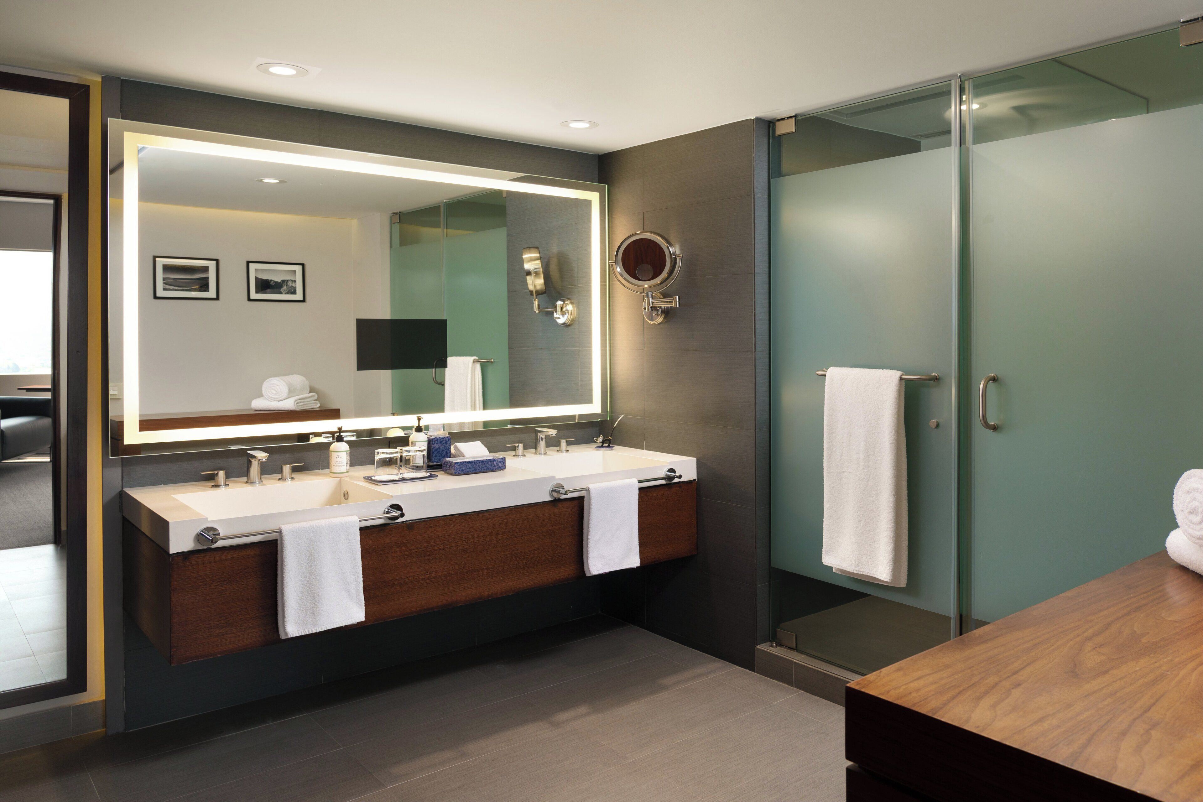 A modern bathroom with a large mirror, dual sinks, and a glass shower enclosure.