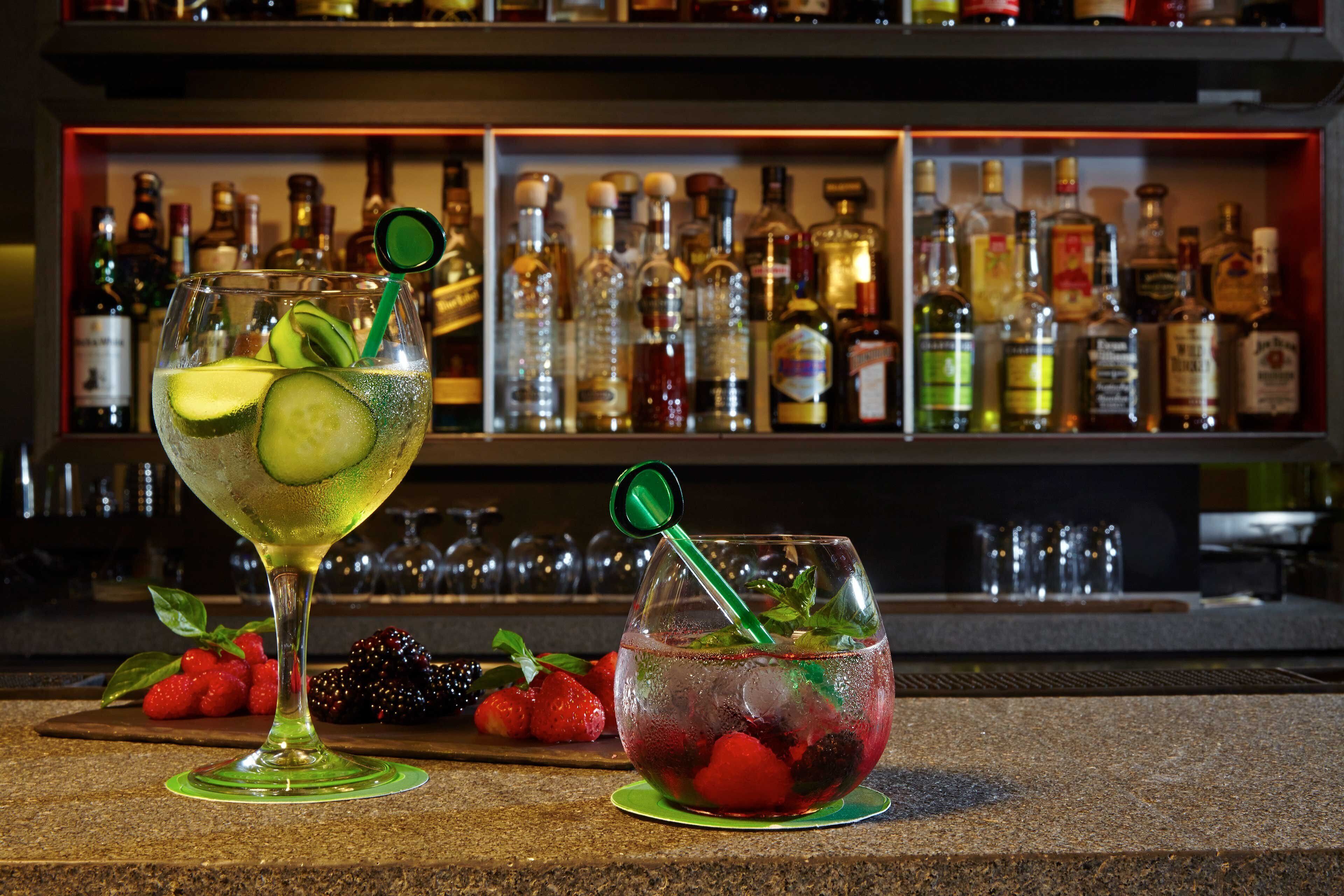 Deux cocktails sur le comptoir d’un bar, avec une variété de bouteilles de spiritueux en arrière-plan.