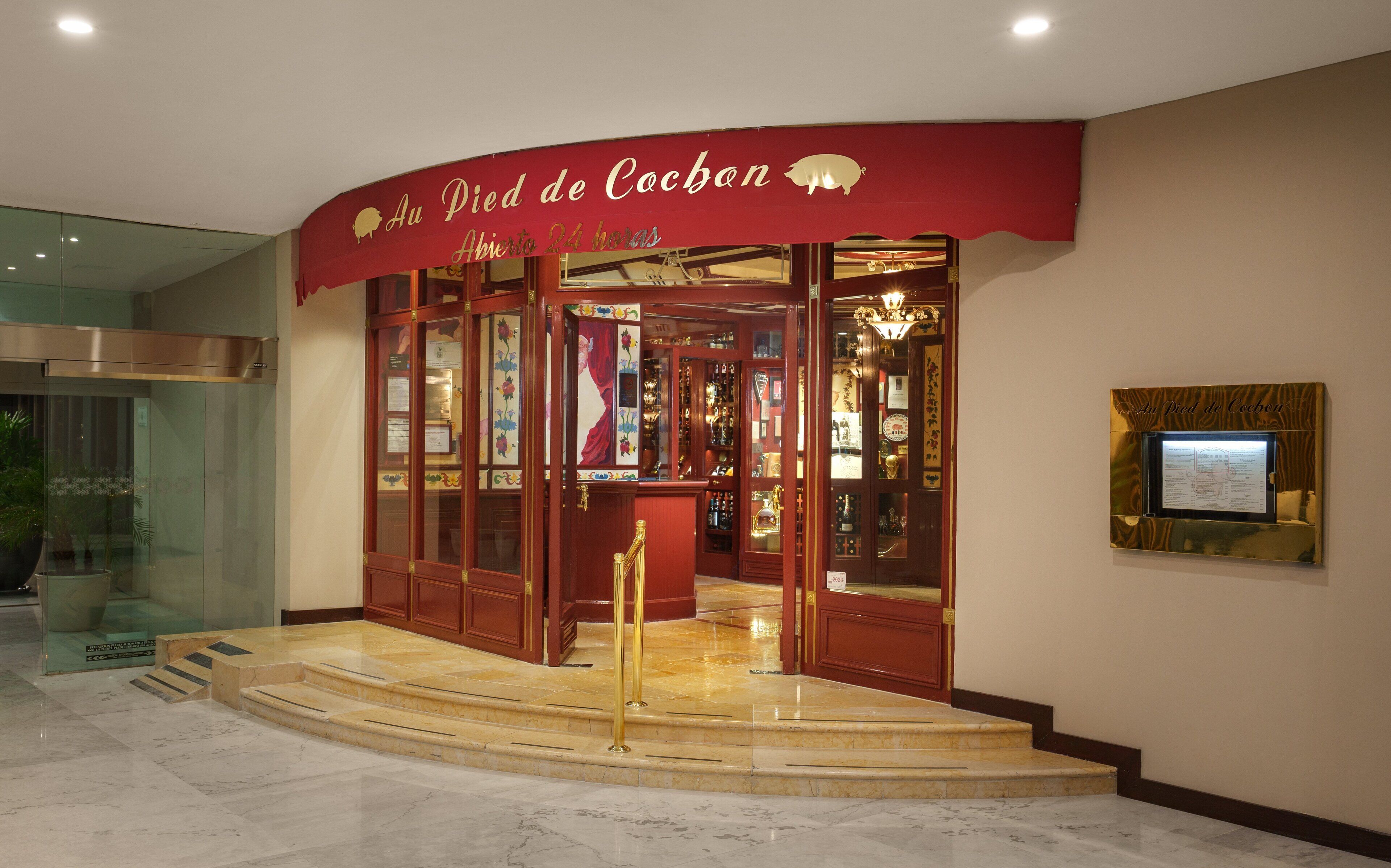 A hotel entrance with a red awning, glass doors, and a display case with items inside.