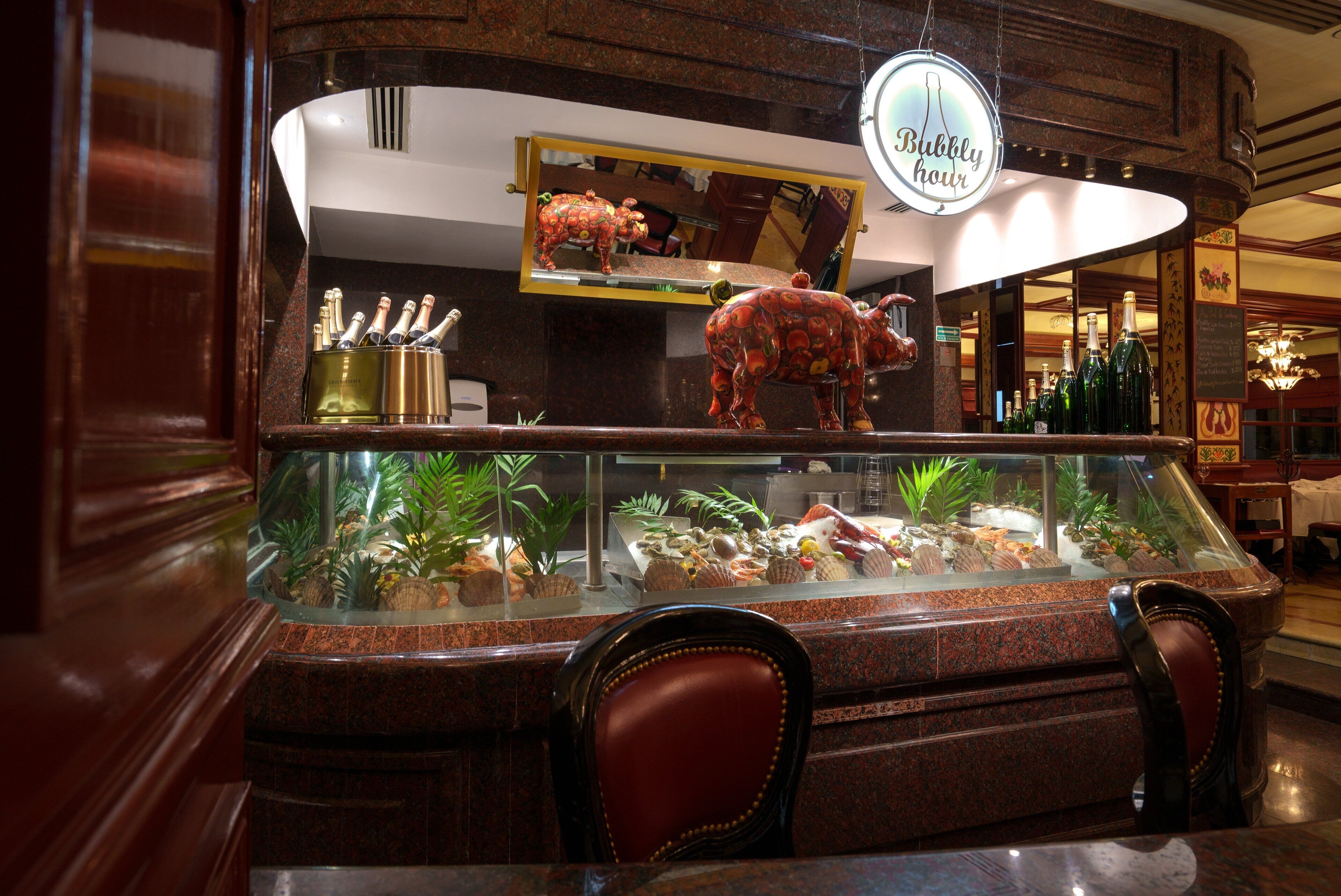 Uma área de bar com uma vitrine de vidro contendo diversos petiscos e um letreiro que diz 'Bubbly Hour'.