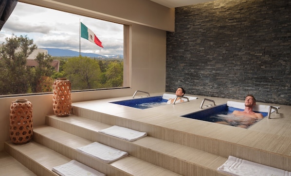 Un área de spa con dos jacuzzis, vista a la ciudad y una pared de piedra.