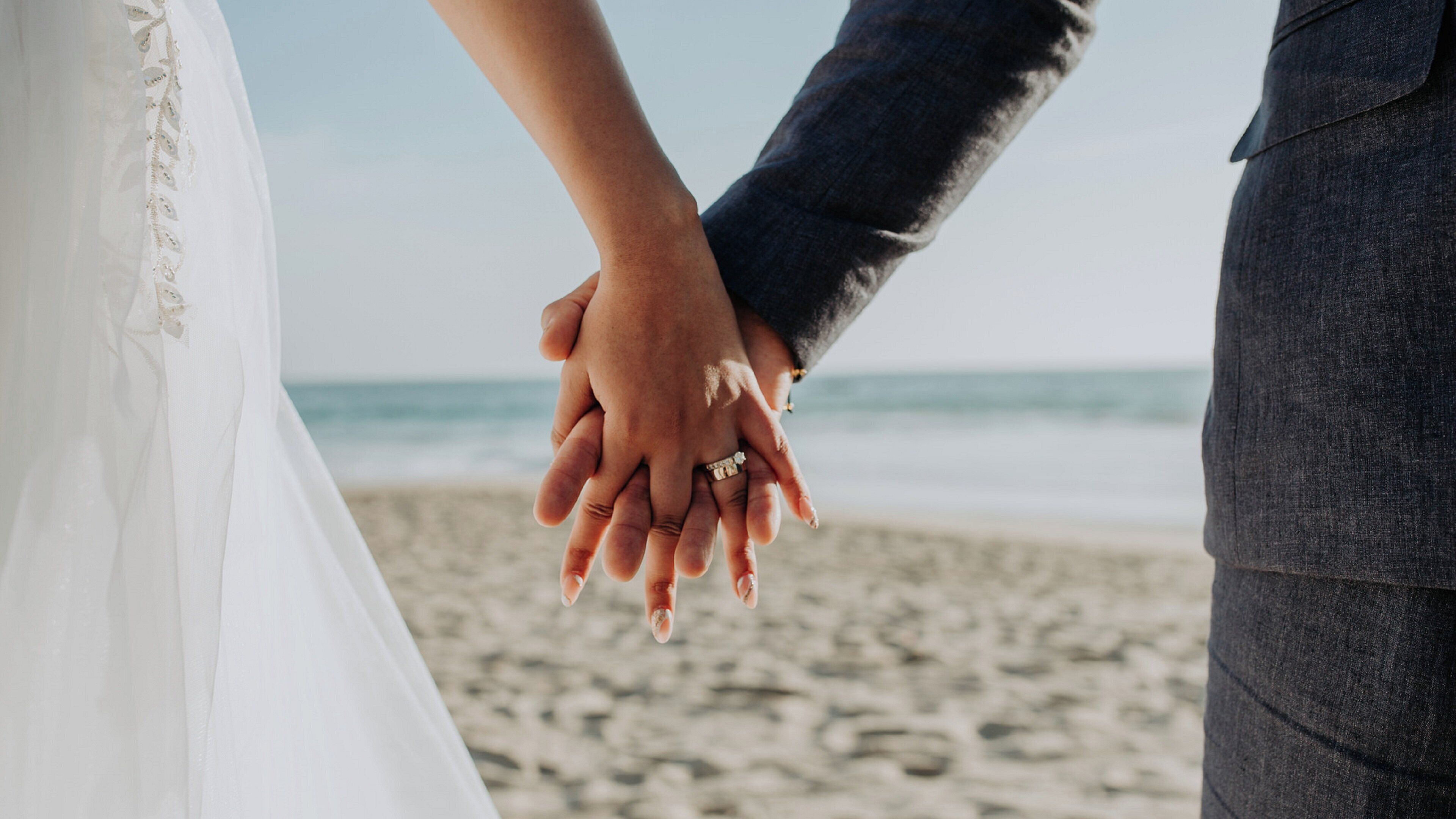 Una pareja tomándose de las manos en una playa con el océano al fondo.