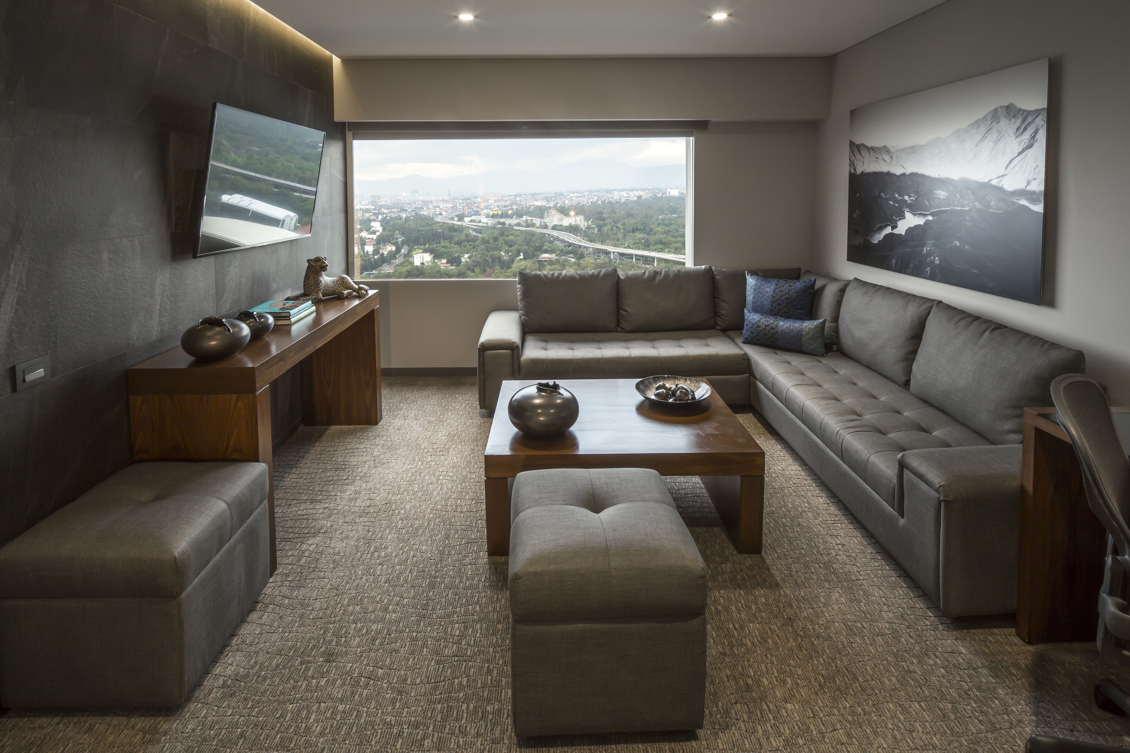 A modern living room with a large window, a sofa, a coffee table, and a TV mounted on the wall.