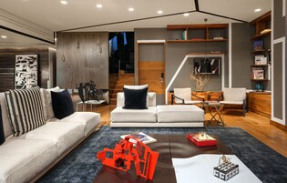 Una sala de estar moderna con sofá, sillones, una mesa de centro y una escalera que lleva a un nivel superior.