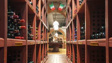 A wine cellar with rows of wine bottles on shelves, a central table, and a brick archway.
