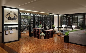 Un interior moderno con una bodega de vinos, suelo de madera y una recepción con asientos y plantas.