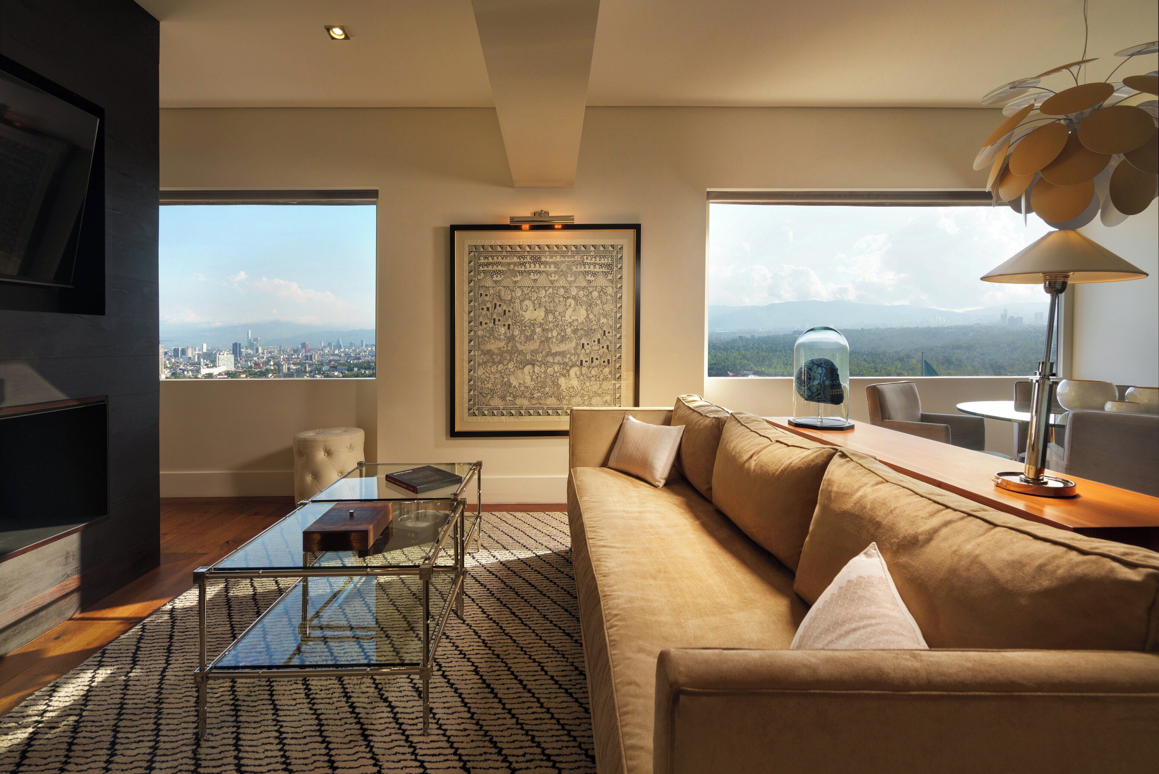 A modern living room with a sofa, coffee table, and a city view through large windows.