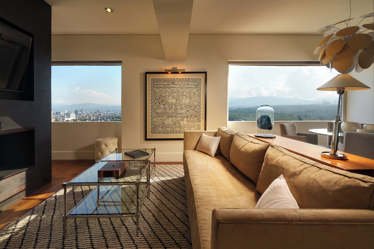 Una sala de estar moderna con sofá, mesa de centro y vista a la ciudad a través de amplios ventanales.