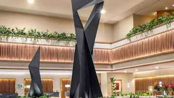 Un lobby amplio con asientos modernos, una escultura negra en el centro y un techo escalonado con plantas.
