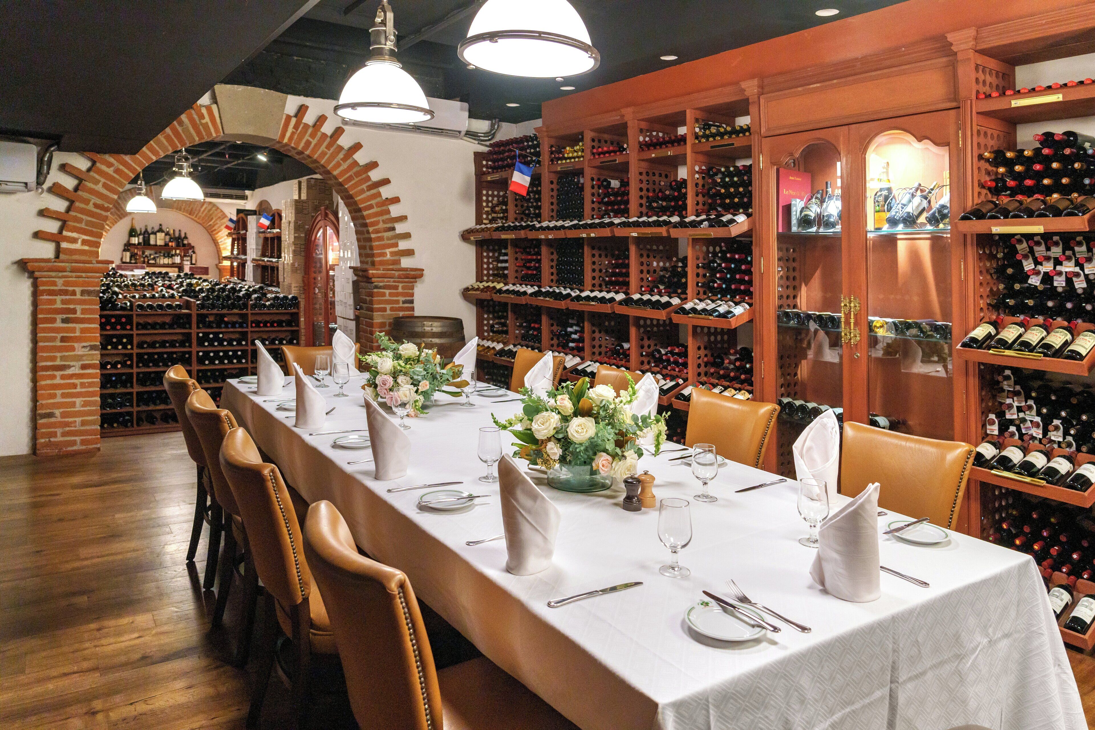 A restaurant with a long table set for dining, surrounded by wine racks and shelves.
