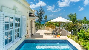 A swimming pool with a tiled edge, a patio area with a white umbrella, and a view of the ocean. - Coral Reef Club (Holetown)