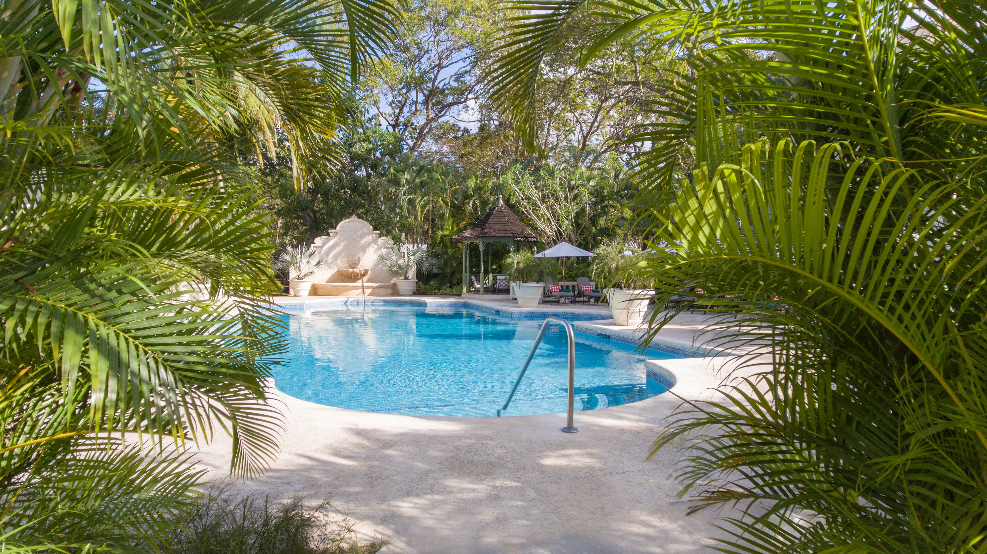 A swimming pool surrounded by palm trees and a gazebo.