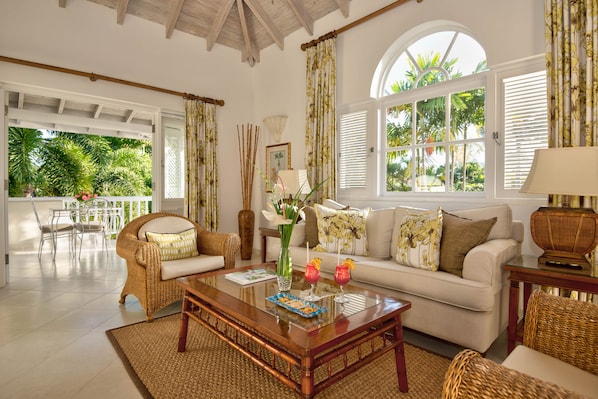 A spacious living room with a sofa, chairs, a coffee table, and large windows with shutters.