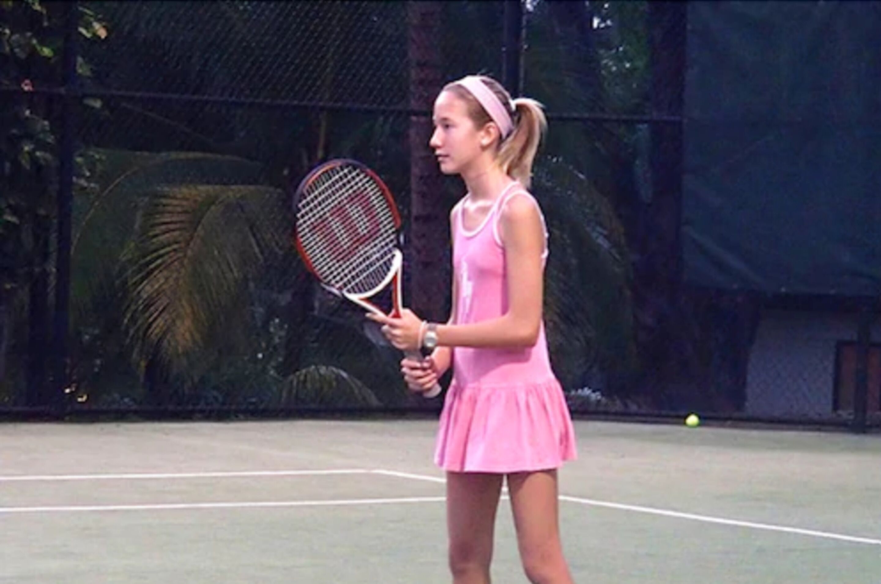 Una cancha de tenis con un jugador con ropa rosa sosteniendo una raqueta.