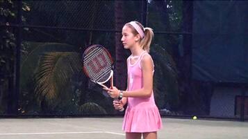 Una cancha de tenis con un jugador con ropa rosa sosteniendo una raqueta.