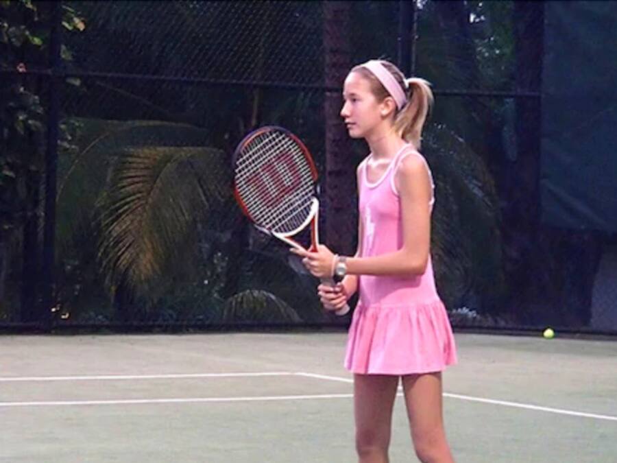 A tennis court with a player in a pink outfit holding a tennis racket.