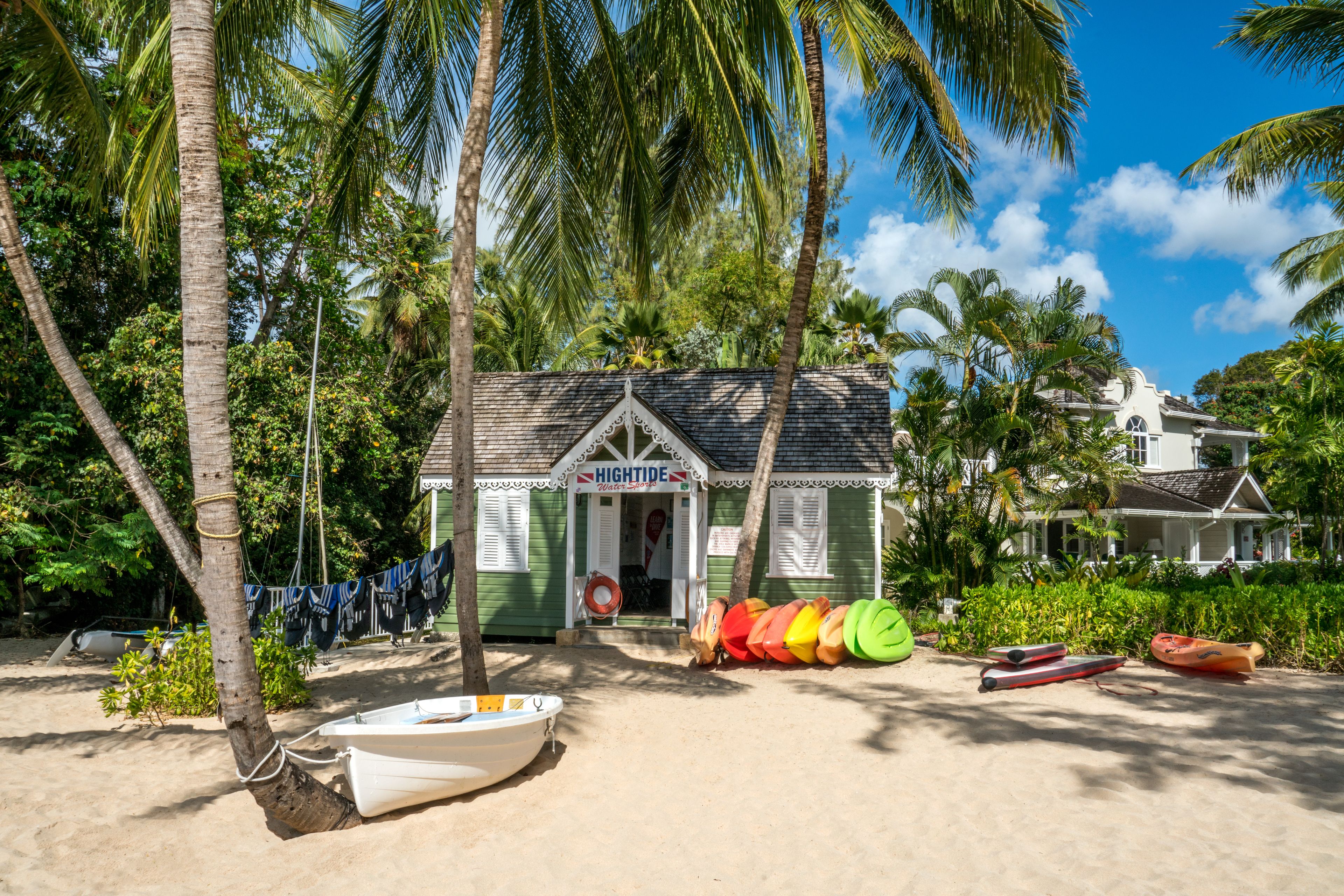 A beachside building with a sign reading "HIGHTIDE," surrounded by palm trees and various colorful kayaks and boats.