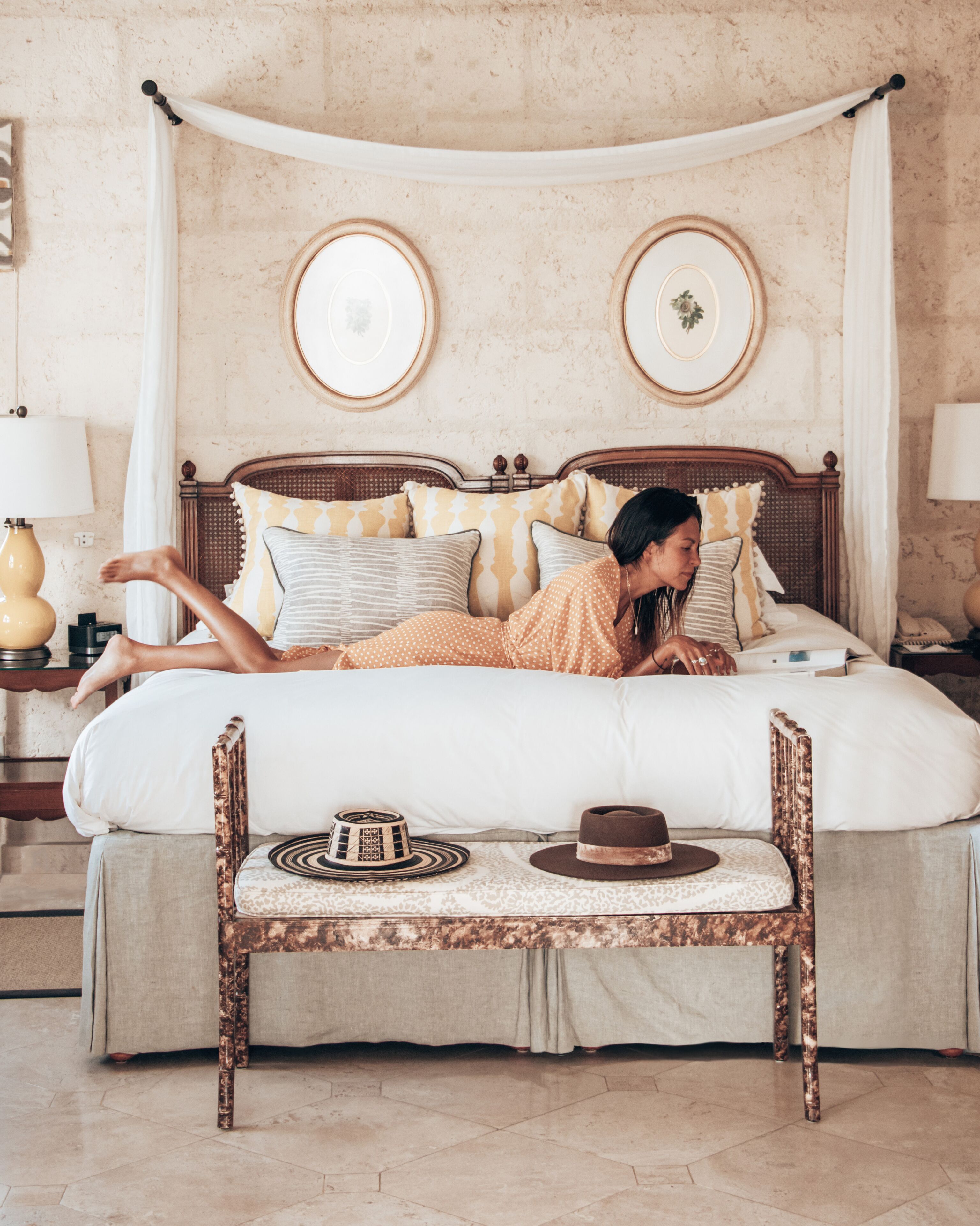 A bed with a canopy, a bedside table, and a chair with a hat and a bowl on it.