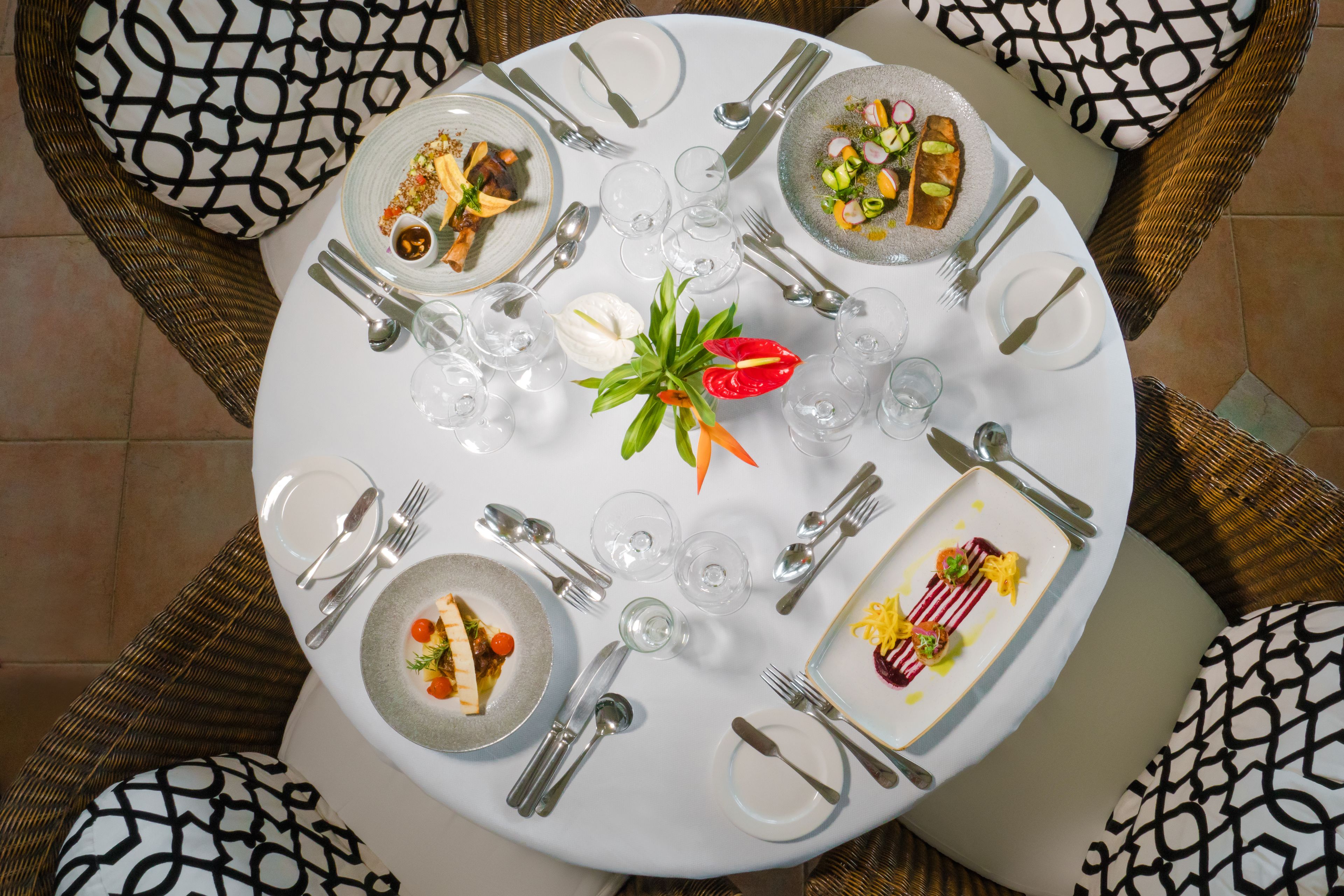 A round dining table set for four with plates of food, cutlery, and glasses.