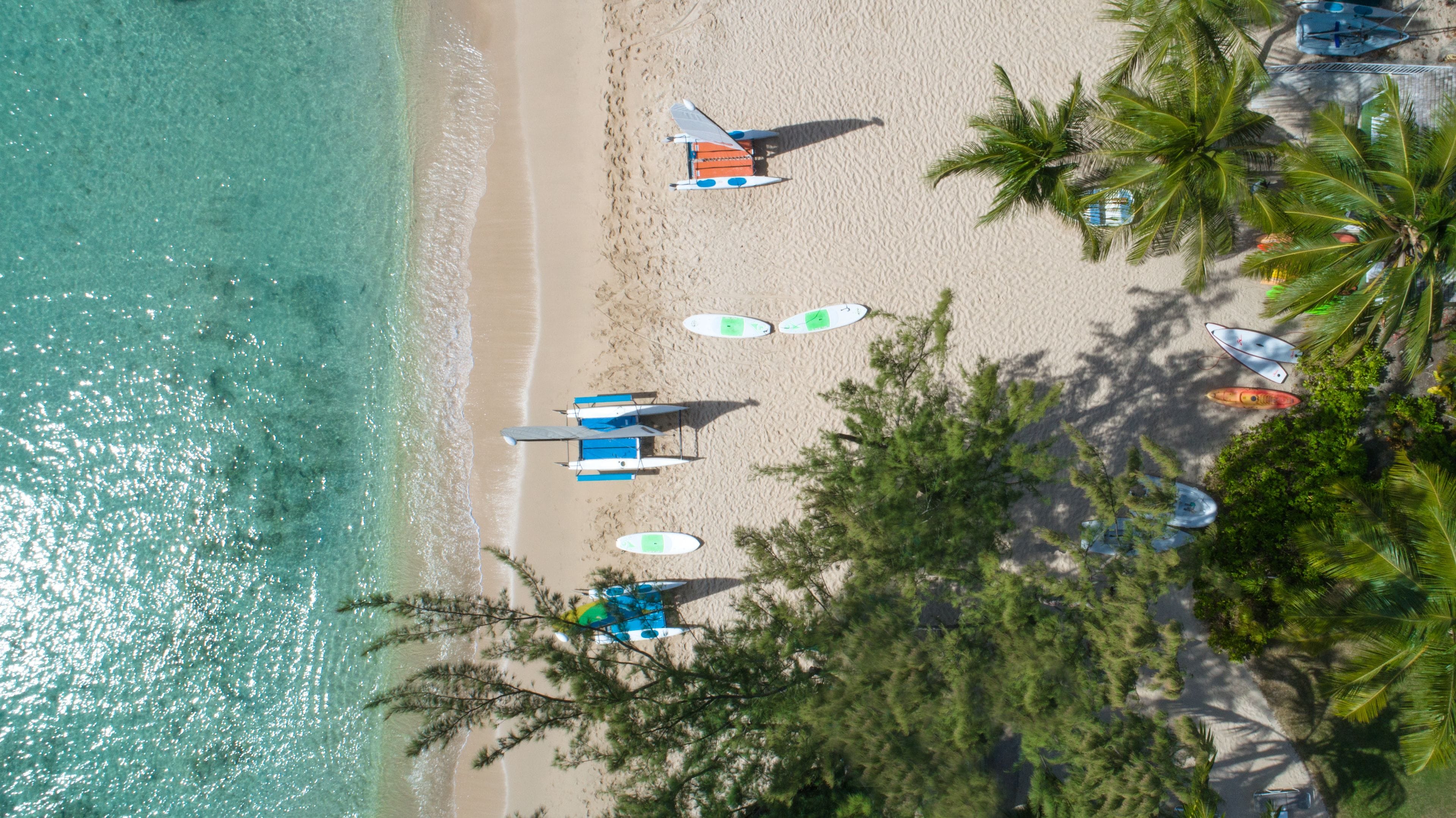 An aerial view of a beach with several surfboards, a beach umbrella, and a small boat.