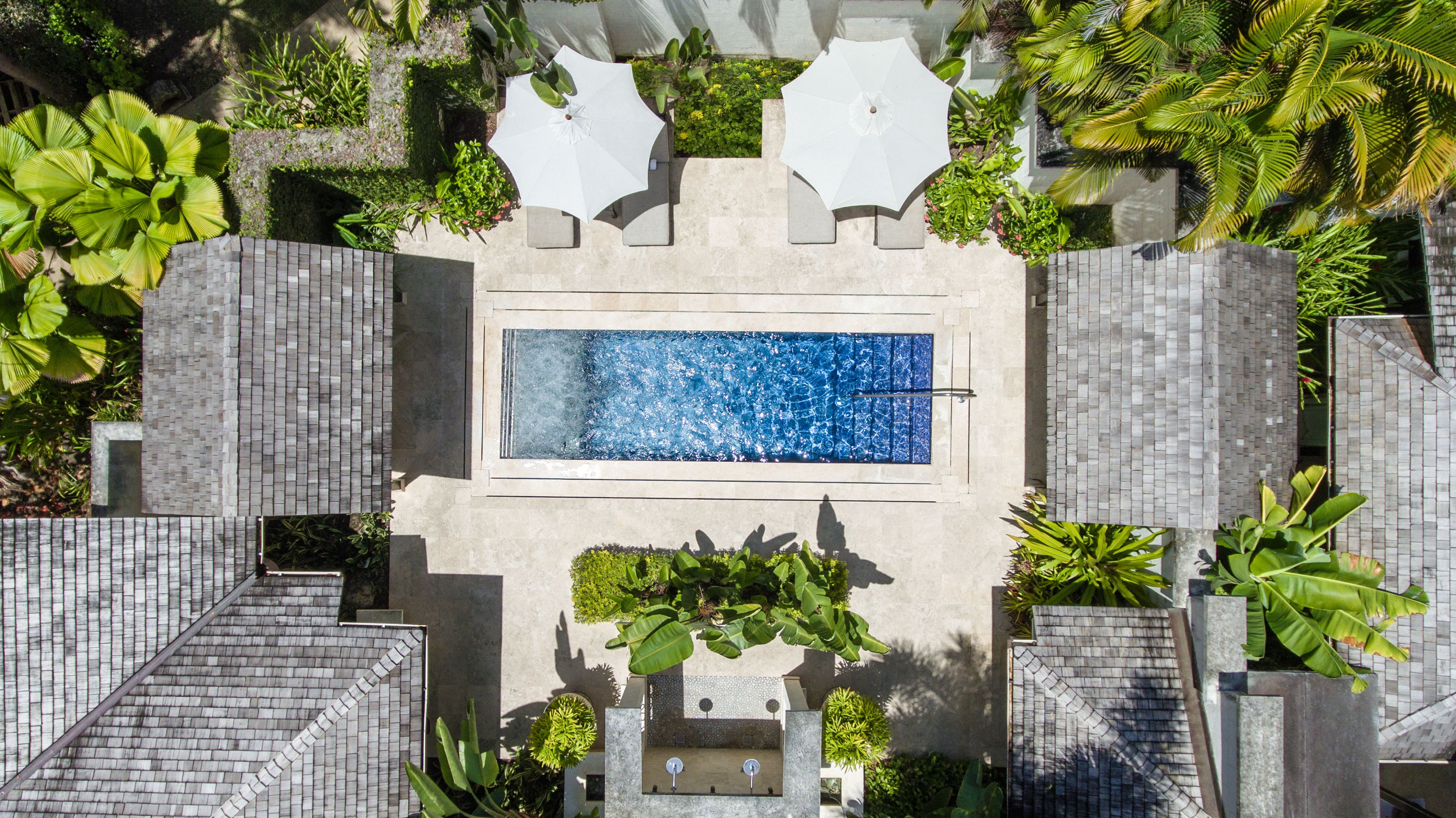 A rectangular pool with a blue mosaic tile design, surrounded by a stone wall and lush greenery.