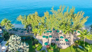 An aerial view of a beach resort with rows of sun loungers and umbrellas, surrounded by palm trees and a clear blue sea. - Coral Reef Club (Holetown)