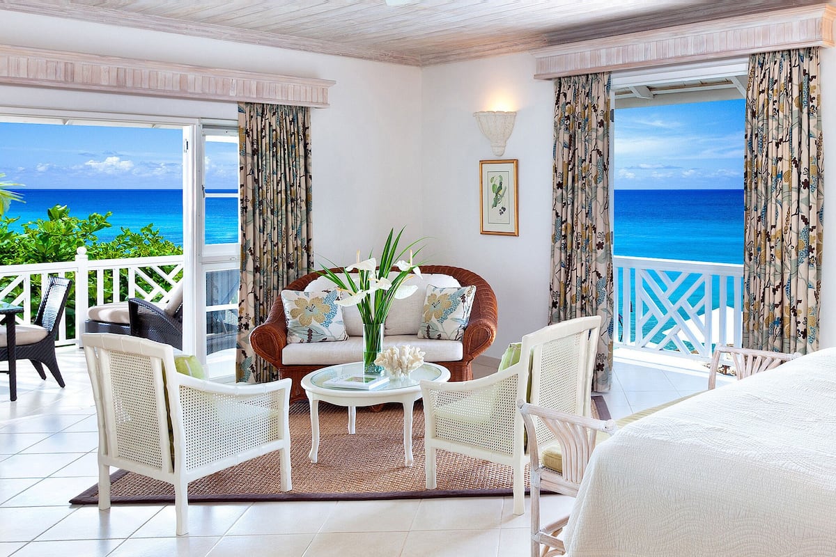 A room with a view of the ocean, white furniture, and a balcony with a white railing.