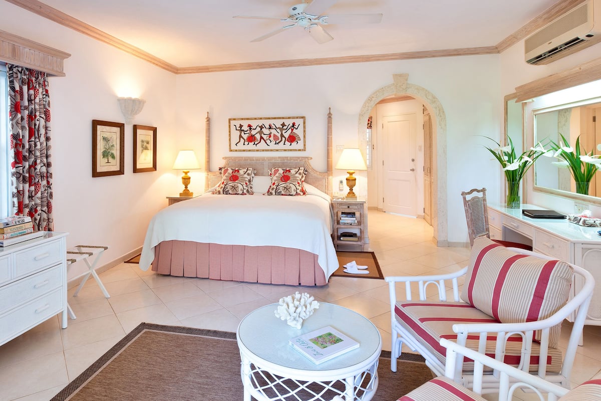 A hotel room with a bed, a desk with a mirror, a chair, a small table, and a ceiling fan.