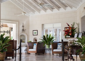 A spacious lobby with high ceilings, a ceiling fan, and a large window. There are several wicker chairs with cushions and a fireplace.