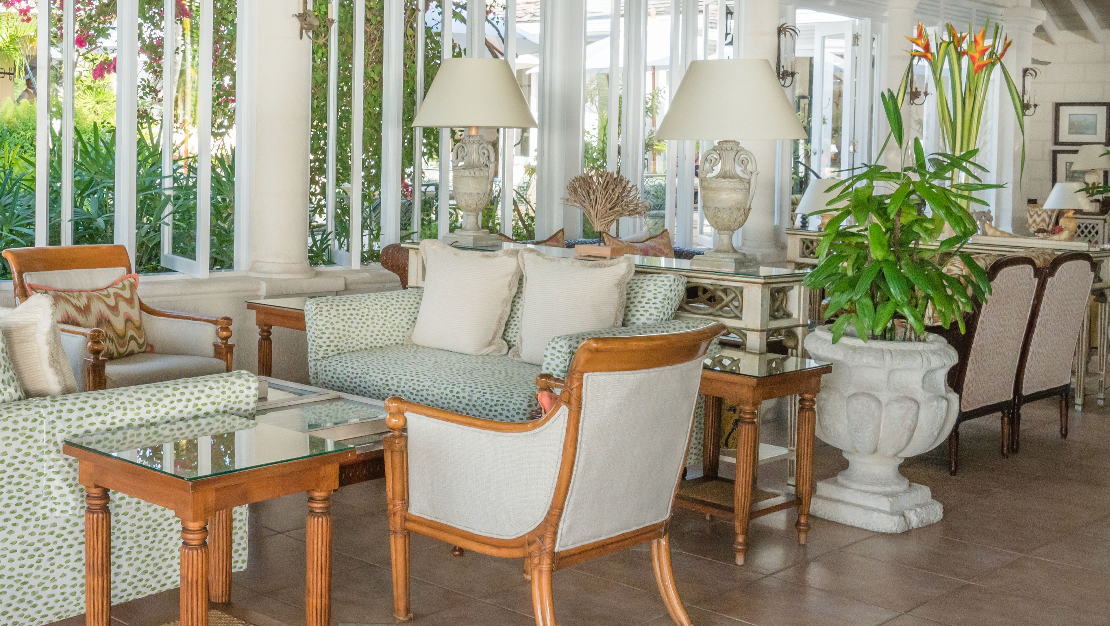 A well-lit, spacious room with a large window, a sofa set, a glass coffee table, and a potted plant.