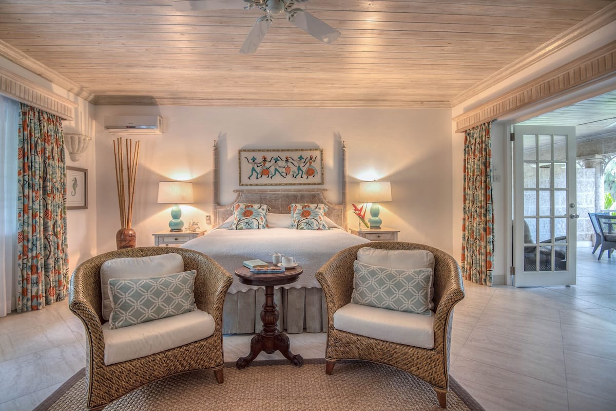 A bedroom with a bed, two wicker chairs, a small table, and a ceiling fan.