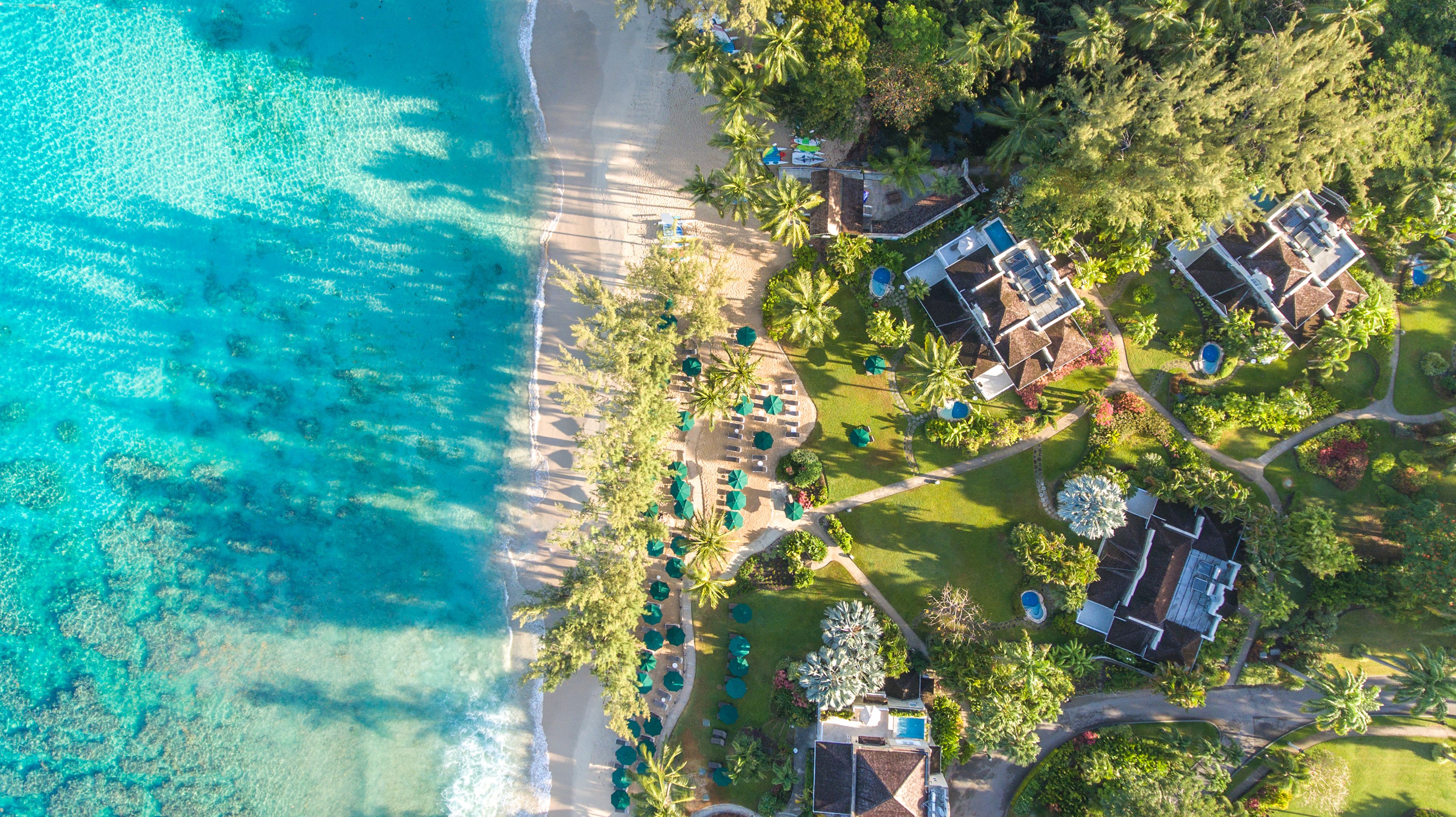 Vista aérea de un complejo turístico con playa, palmeras y zona de piscina.
