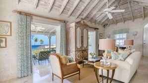 A spacious living room with a high ceiling, a large wooden cabinet, a white sofa, and a glass coffee table. - Coral Reef Club (Holetown)