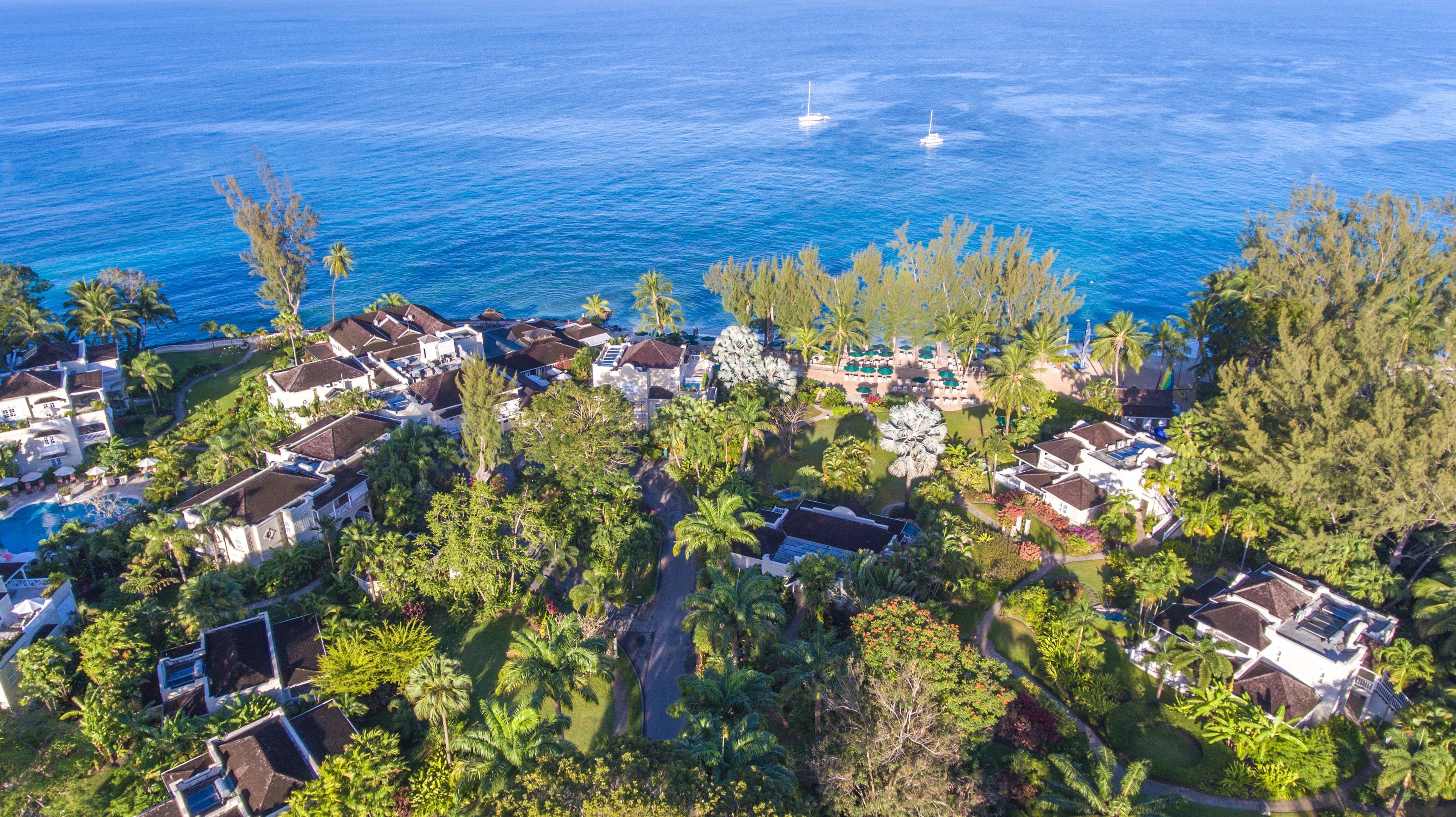 An aerial view of a coastal resort with multiple bungalow-style buildings, a central pool area, and a view of the ocean.