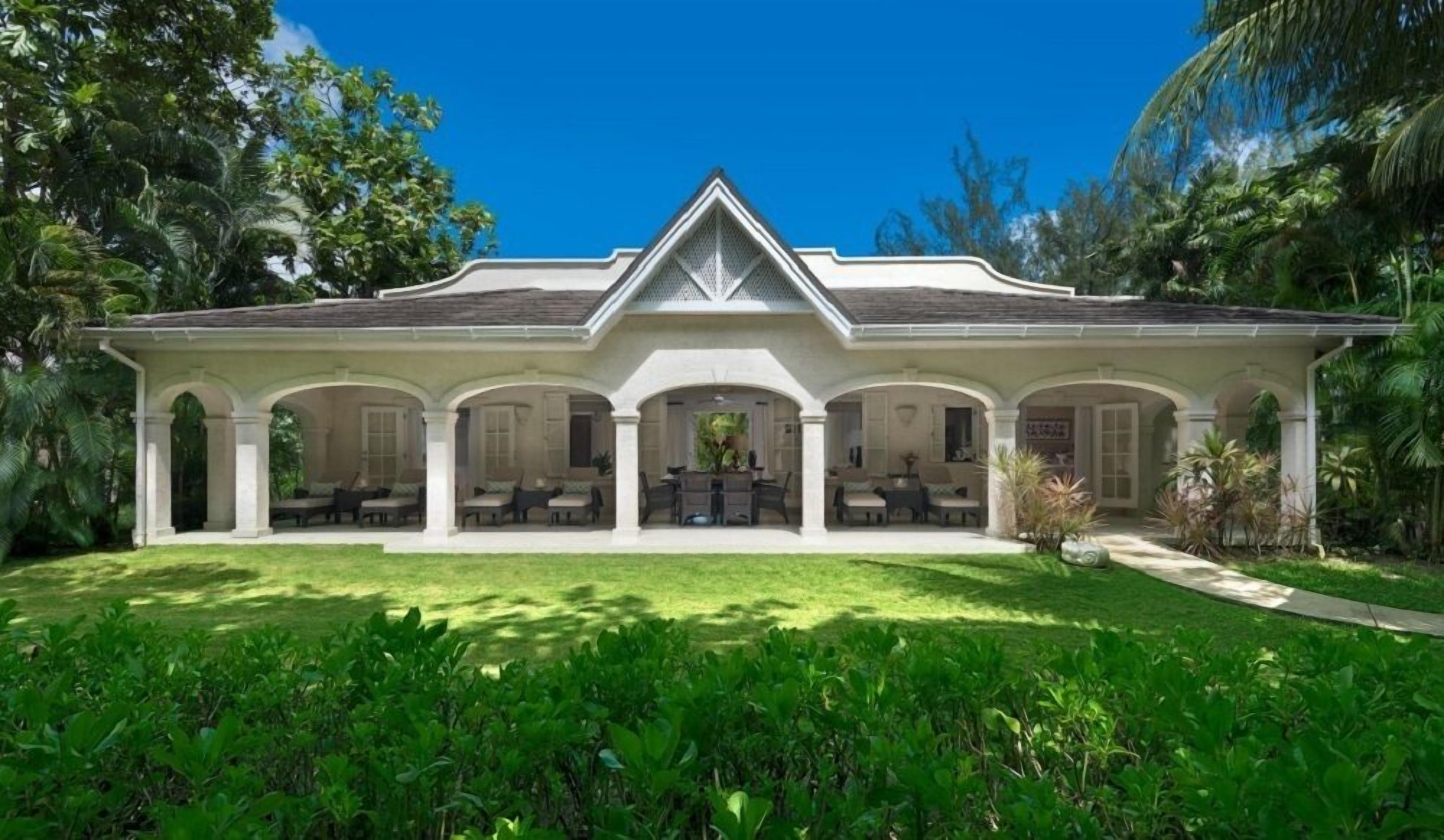 A large, two-story house with a covered patio area featuring multiple seating arrangements and a central dining table.