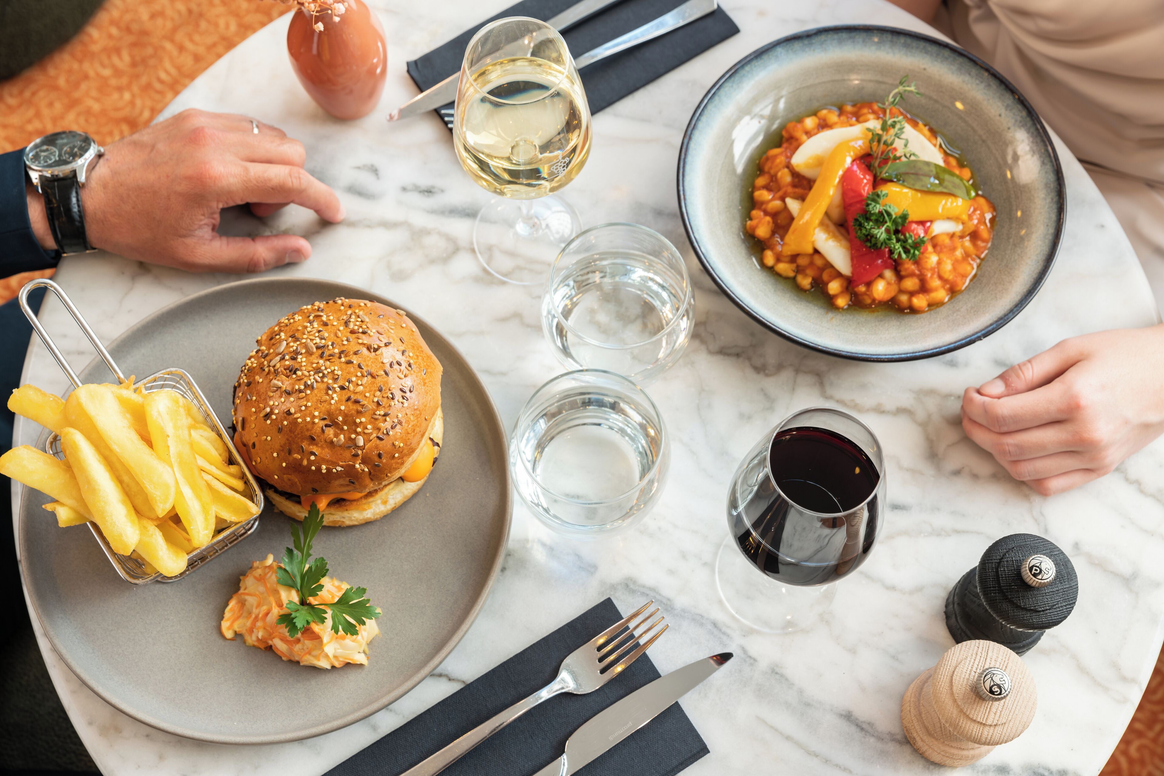 A dining table with a burger, fries, and a bowl of beans.