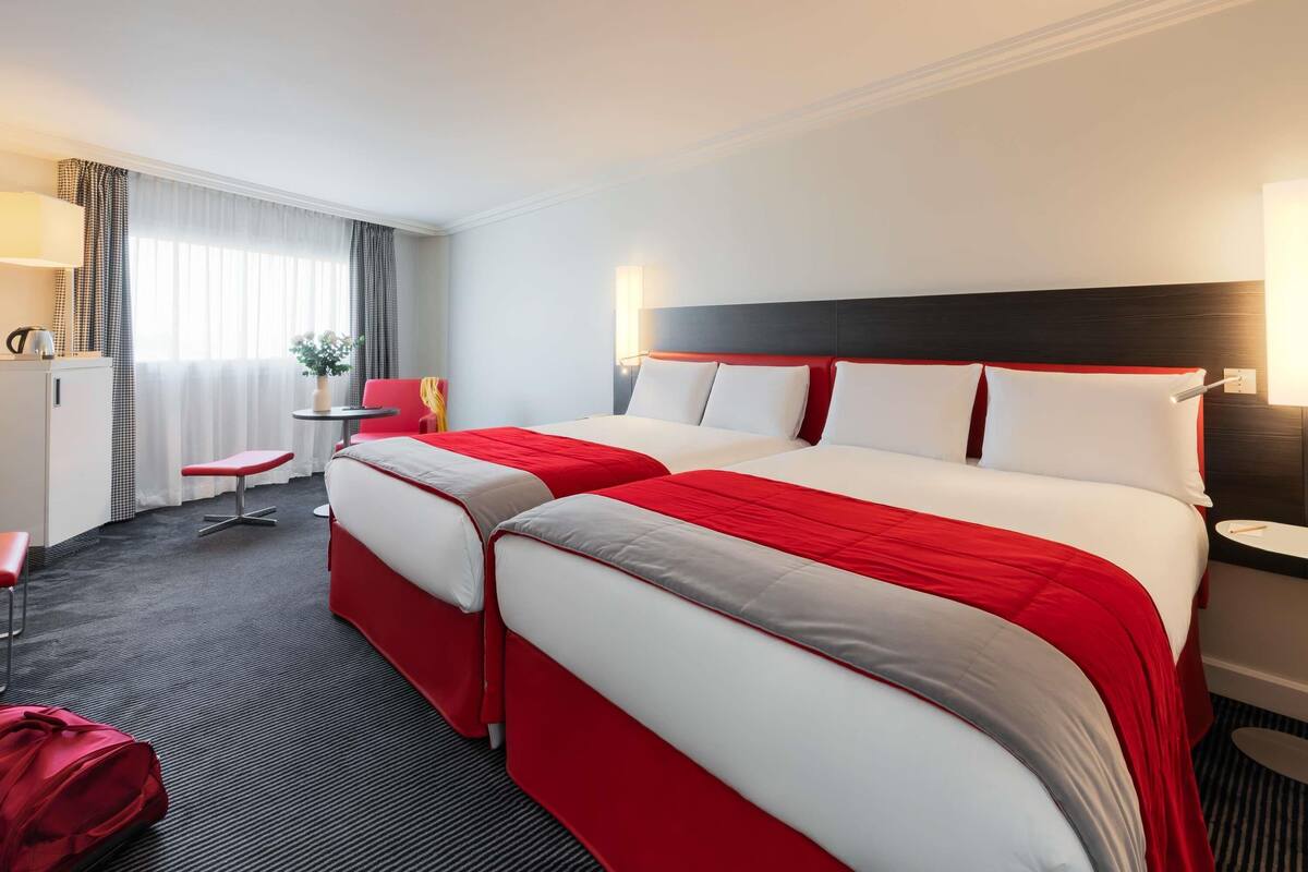 A hotel room with two beds, a desk, a chair, and a small table.