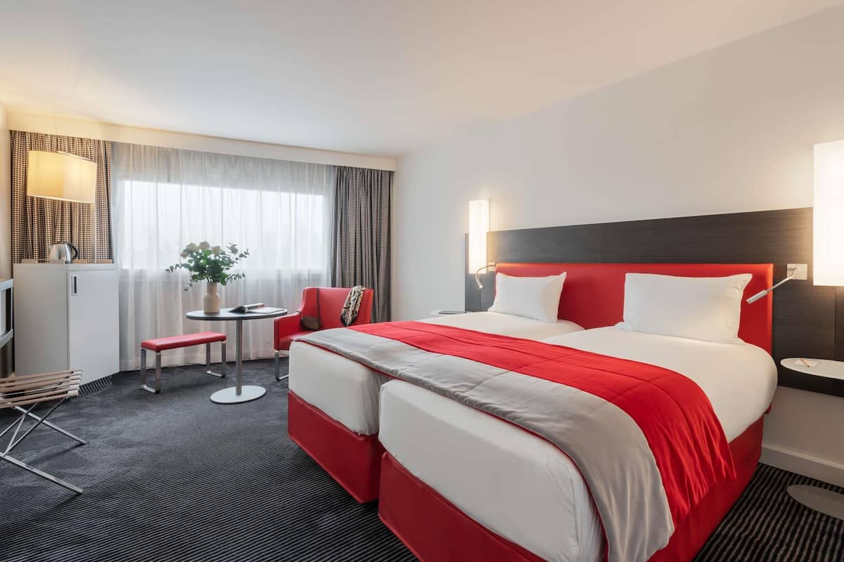 A hotel room with a large bed, a desk, a chair, and a small table.