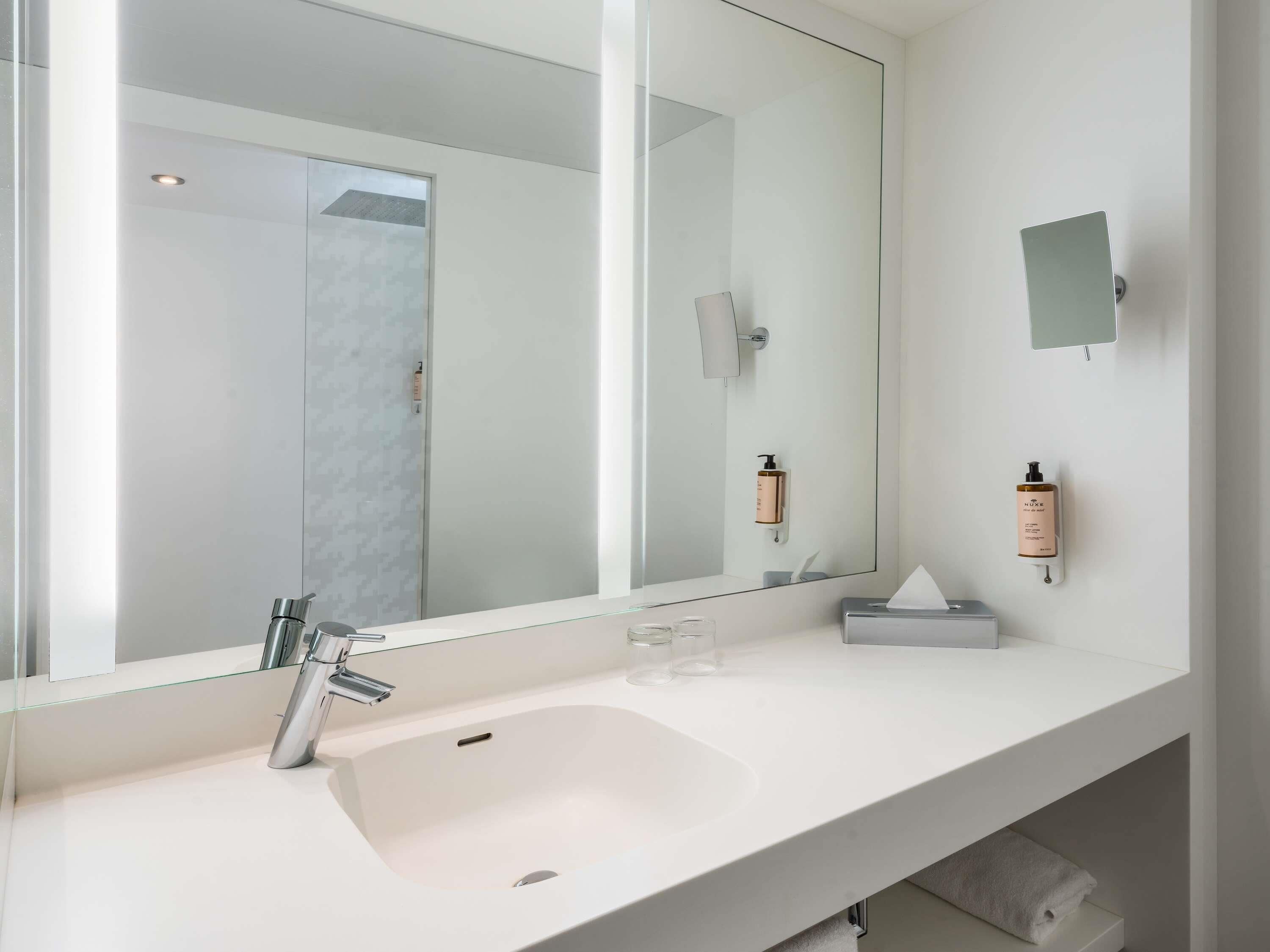 A modern bathroom with a large mirror, a white sink, and two wall-mounted soap dispensers.